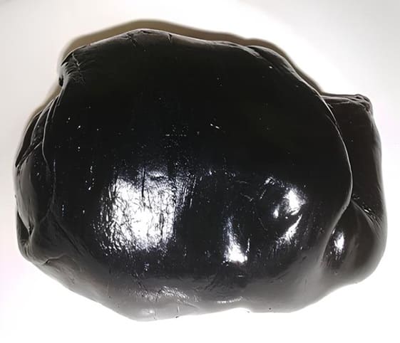 Bitumen / Shilajit A black rock, identified as bitumen or shilajit, rests on a smooth white surface.