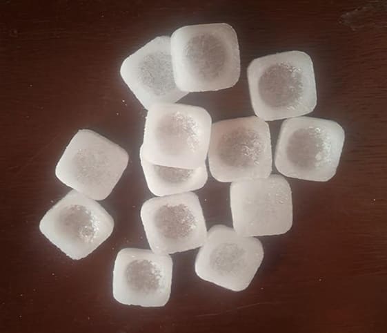 Camphor A neatly arranged pile of camphor cubes resting on a wooden table surface.