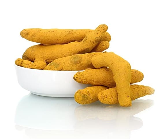 Dried Turmeric A bowl filled with vibrant yellow dried turmeric fingers placed on a clean white surface.