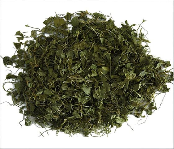Dry Fenugreek Leaves A close-up view of a pile of dried fenugreek leaves resting on a clean white surface.