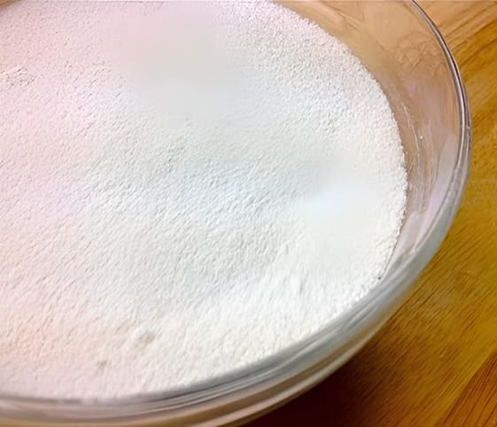 Dust Sugar A bowl of white sugar powder placed on a rustic wooden table.