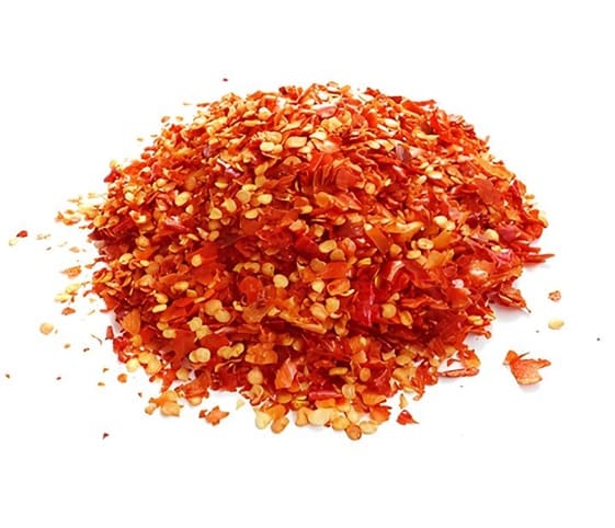 Red Chilli Flakes A mound of bright red chili flakes displayed on a plain white surface.