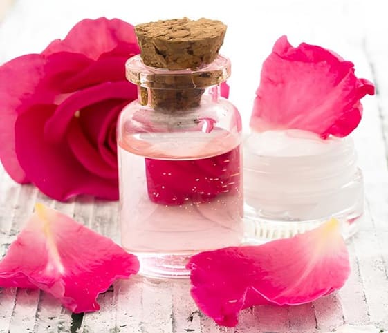Rose Water A glass bottle filled with rose essential oil surrounded by delicate rose petals.