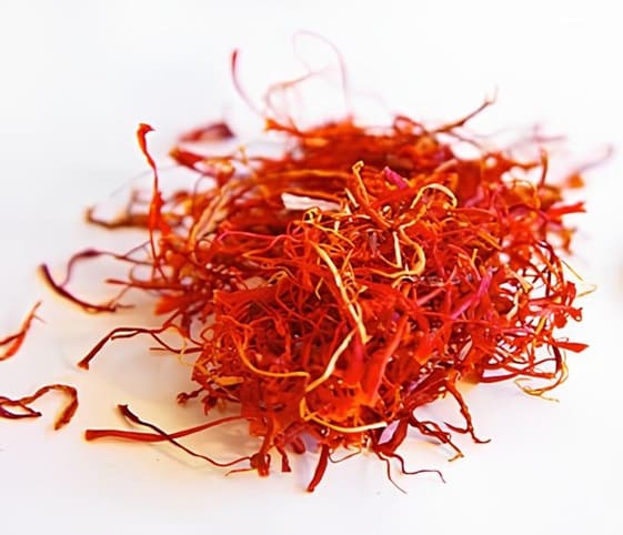 Saffron A close-up view of a pile of vibrant saffron threads resting on a clean white surface.